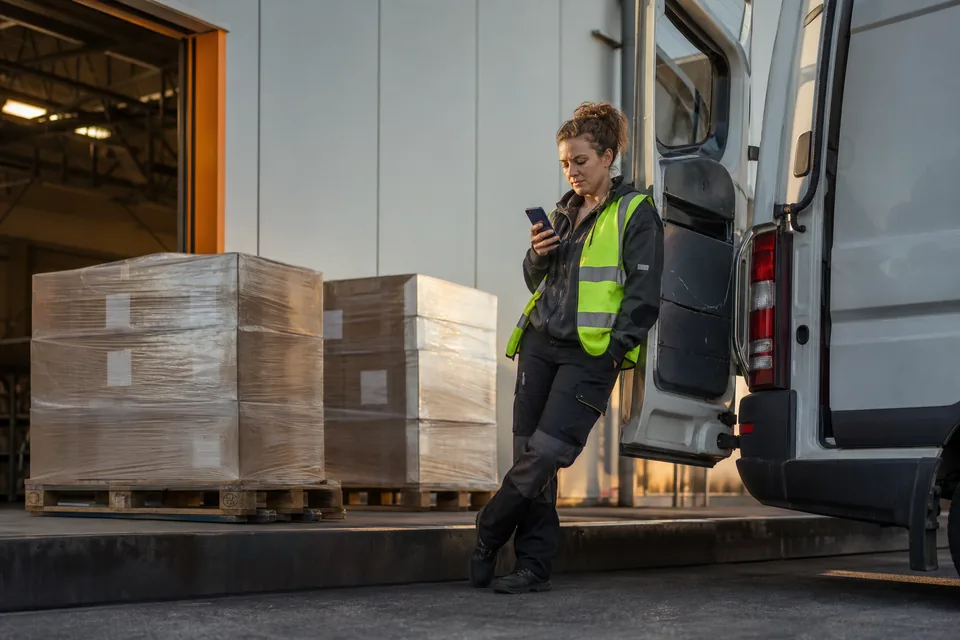 Kierowczyni busa do 3,5 t sprawdza ładunki w telefonie przy rampie magazynu